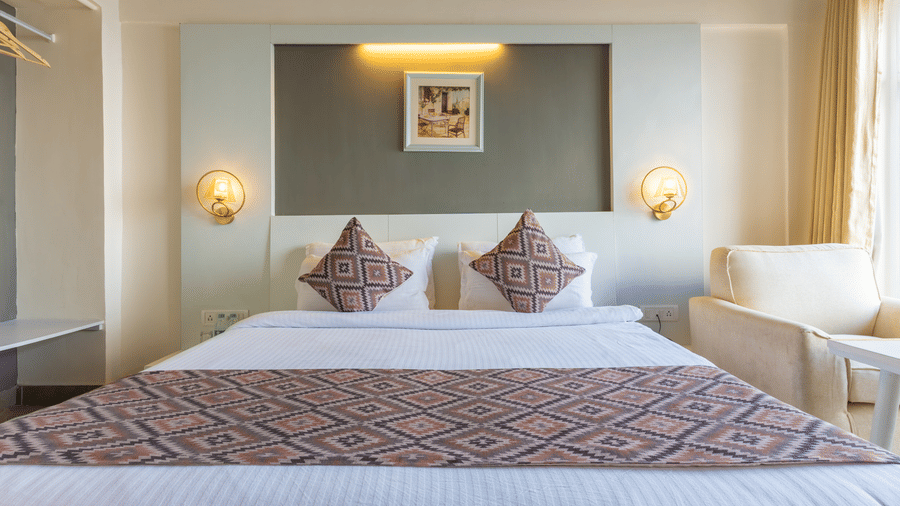 Front-facing view of a double bed with two pillows and an armchair placed by the window at Himalayas Resort By The Lake Hill, Mukteshwar.