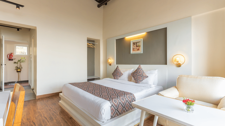 Spacious guest room with a double bed, white linens, and a white coffee table with an armchair at Himalayas Resort By The Lake Hill, Mukteshwar.