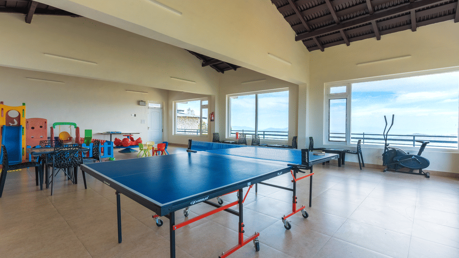 A recreation room featuring a blue table tennis table and gym equipment next to large windows at Himalayas Resort By The Lake Hill, Mukteshwar.