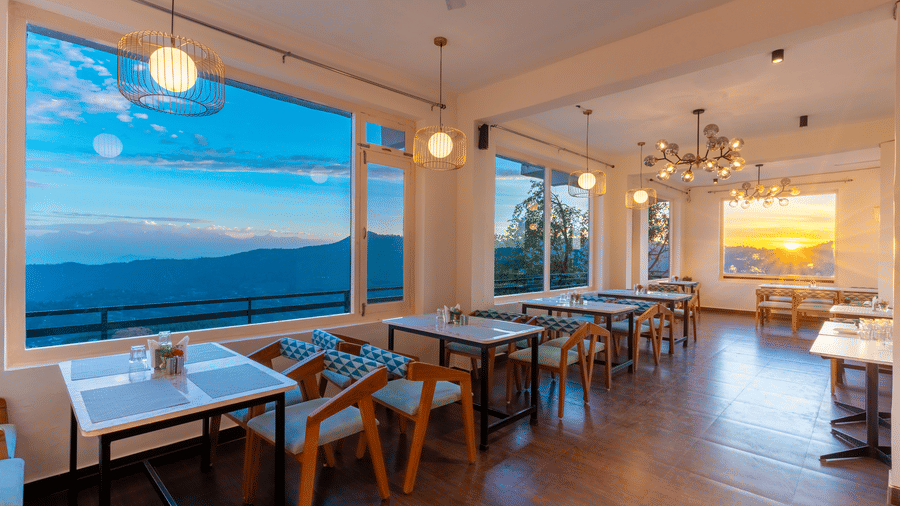 A modern dining room with wooden tables and large windows offering a panoramic sunset view at Himalayas Resort By The Lake Hill, Mukteshwar.