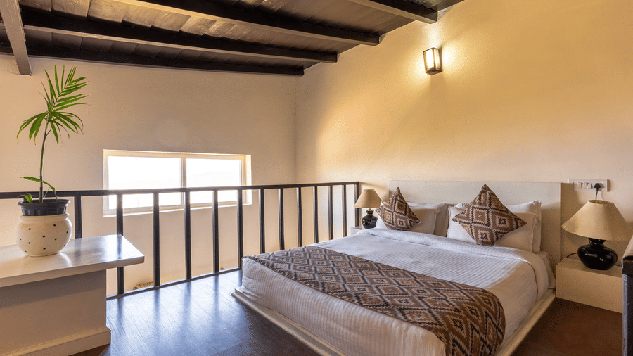 A loft-style bedroom with a dark wooden slanted ceiling, white bed linens, and a black railing at Himalayas Resort By The Lake Hill, Mukteshwar.