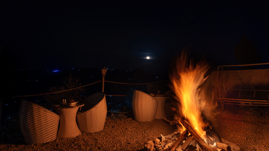 A warm bonfire burning in an outdoor seating area with white chairs under a dark night sky at Himalayas Resort By The Lake Hill, Mukteshwar.
