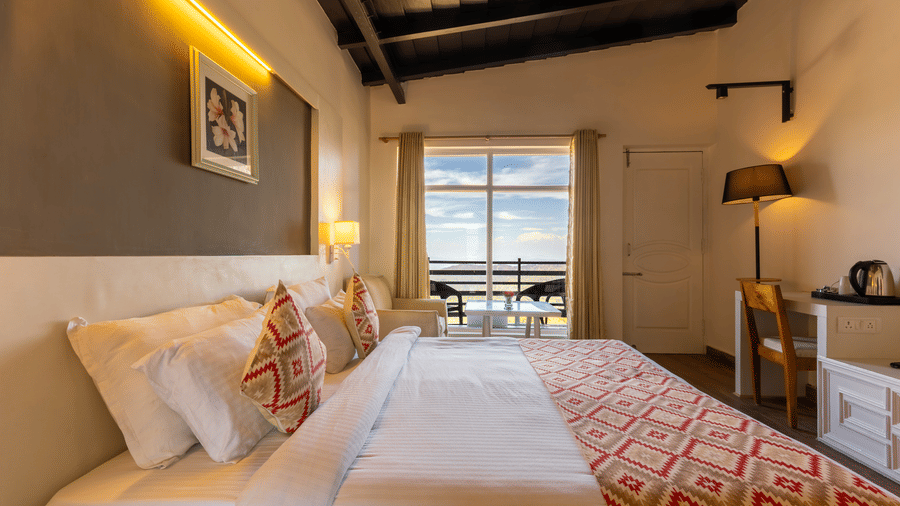 Bedroom with a large bed, patterned runner, and a large window showing a balcony view at Himalayas Resort By The Lake Hill, Mukteshwar.