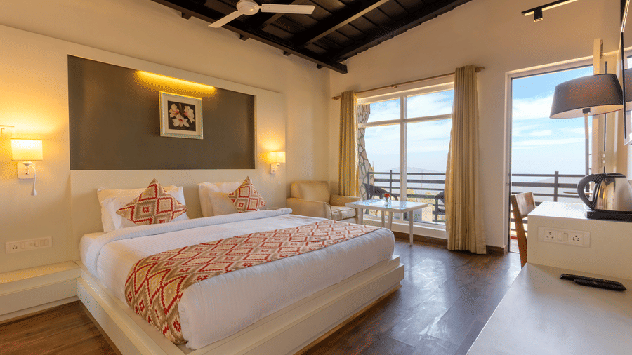 Bedroom featuring a bed with a patterned throw, a white desk, and a balcony window at Himalayas Resort By The Lake Hill, Mukteshwar.