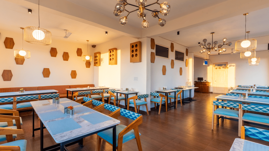 A well-lit dining area with wooden tables and blue chairs under modern gold-tone chandeliers at Himalayas Resort By The Lake Hill, Mukteshwar.