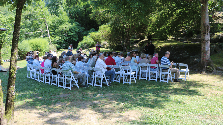 a group of people gathered together sitting on the white colored chairs under a tree shade surrounded by lush greenery - Historic Tapoco Lodge