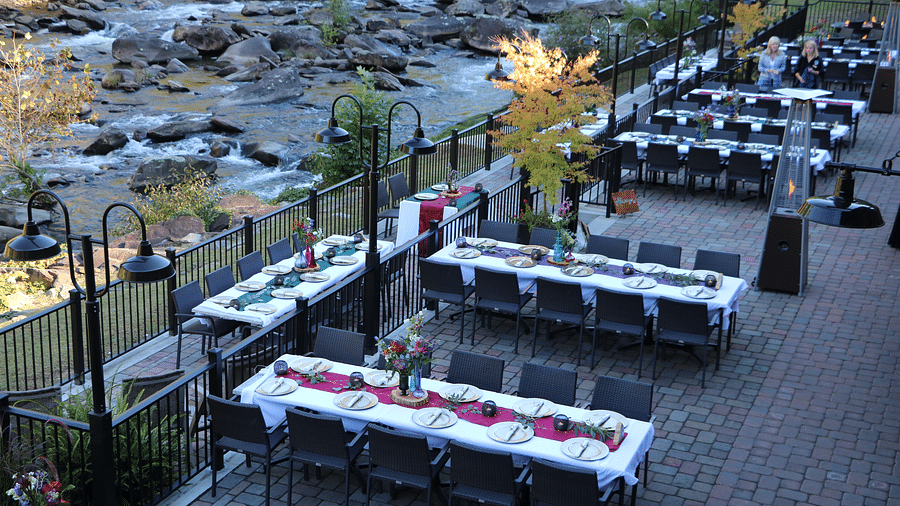 the riverside dining setup taken from an elevation with neatly arranged tables and chairs along a bricked pathway - Historic Tapoco Lodge
