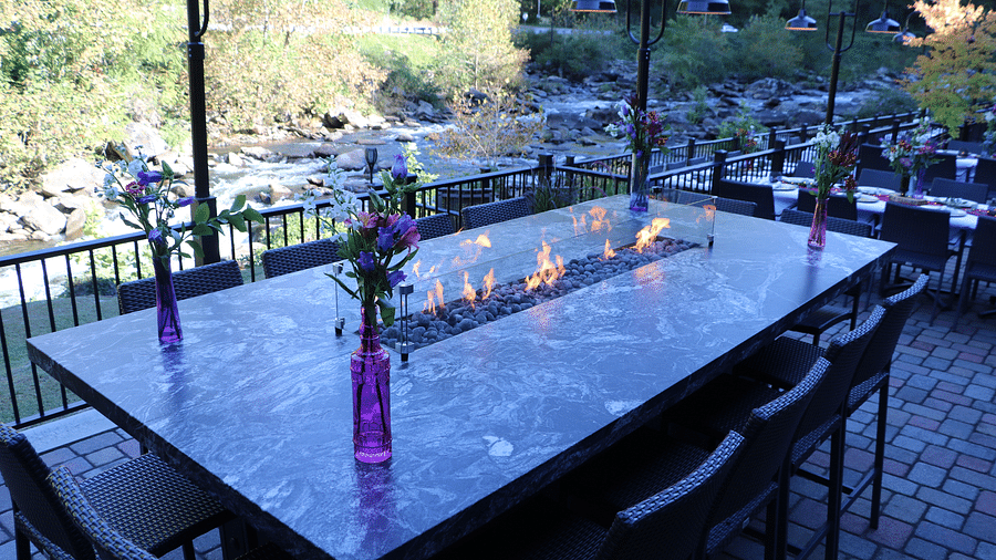 corner view image of a long marble dining table surrounded by black colored chairs overlooking the thorny bushes in the background - Historic Tapoco Lodge