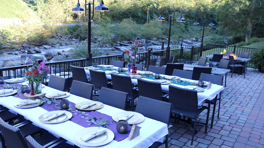 an outdoor dining space with a fire pit, floral arrangements, and a covered patio in the background - Historic Tapoco Lodge