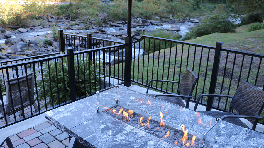 a marble dining table with stone fire pit surrounded with chairs facing towards the river - Historic Tapoco Lodge