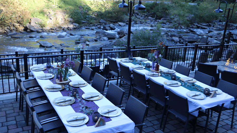 long dining tables places alongside the hand railings covered with white colored table cloth overlooking the river besides it - Historic Tapoco Lodge