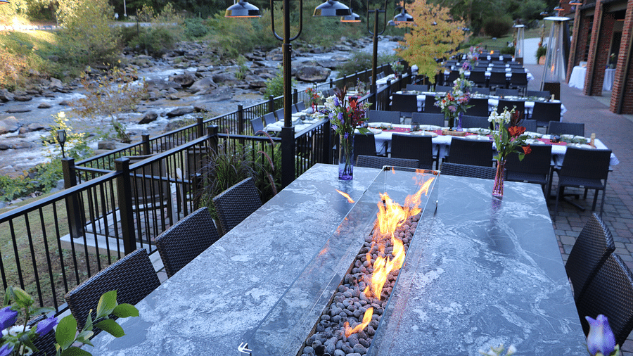 a stone fire pit surrounded by dining tables overlooking the river and greenery - Historic Tapoco Lodge