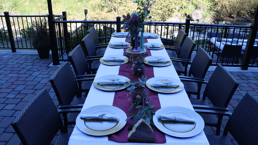 a long dining table set with plates, cutlery, and a purple table runner overlooking the river - Historic Tapoco Lodge