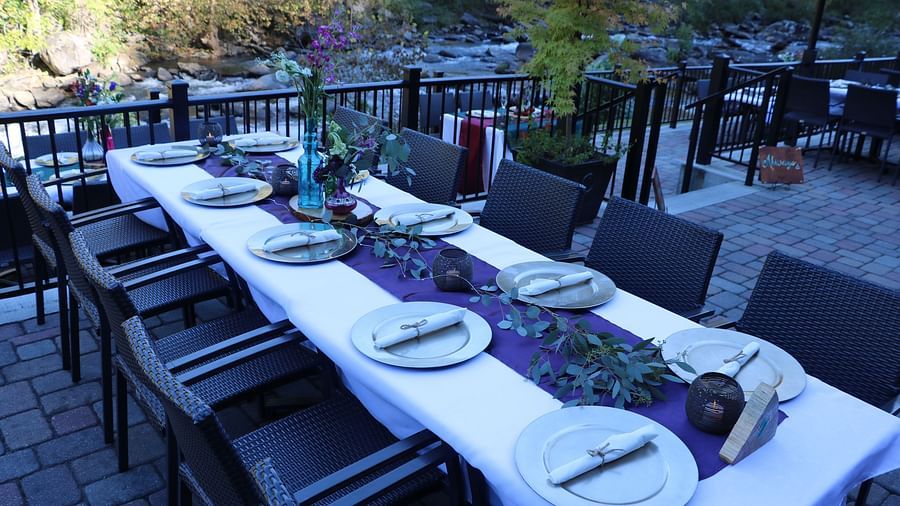 corner view of the outdoor dining area featuring a table with a white table cloth, black chairs, and a riverside view - Historic Tapoco Lodge