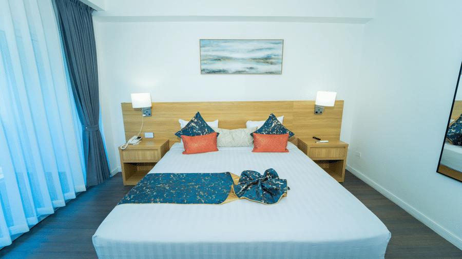 Plush king size bed with warm-toned night lamps on wooden bedside tables in a room with cream walls and soft white linens | Hotel 39 - Hotel in Montego Bay