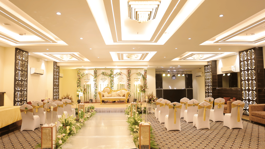 A grand banquet hall arranged with white-covered chairs in a theatre-style setup facing a decorated event stage - Hotel 91 HUDA City Centre, Gurugram