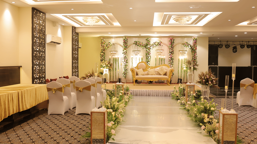 An elegant wedding stage decorated with fresh floral arrangements and a white runner leading to a golden ornamental sofa - Hotel 91 HUDA City Centre, Gurugram