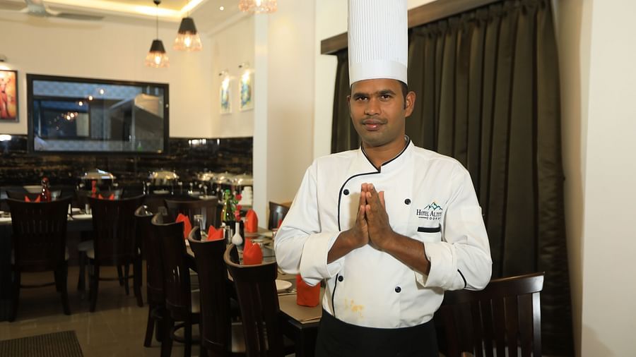 Image of a man posing for a photograph with tables and chairs in the background at Hotel Altitude, Madikeri.