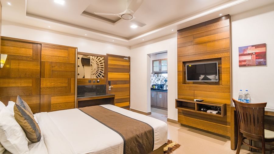 Image of a room with a bed, a television, a table, and a chair in front at Hotel Altitude, Madikeri.