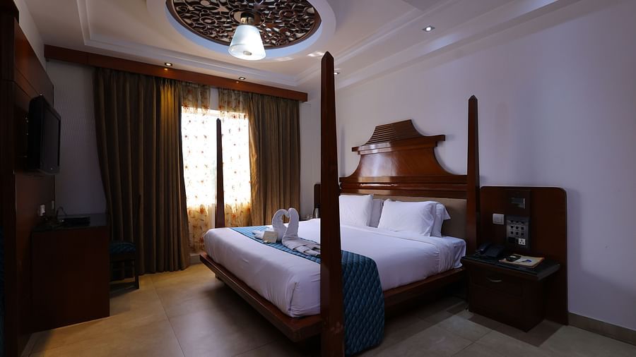 Image of Premium room at Hotel Amar with a bed, sofa, side table and long curtains.