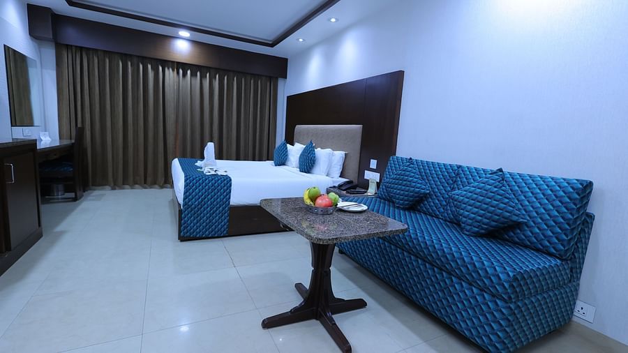 Image of Premium room at Hotel Amar with a bed, sofa, table and long curtains.
