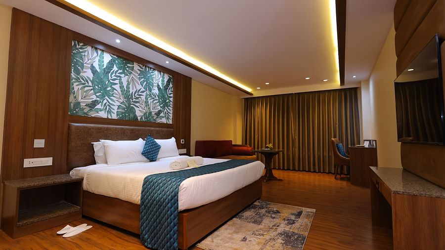 Side angle image of a Suite at Amar Hotel with a bed, table, TV and a painting
