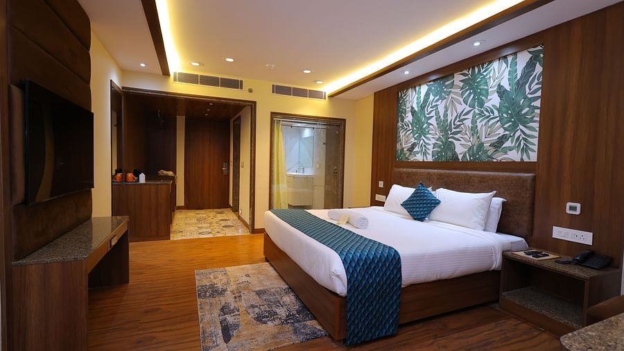 Side angle image of a Suite at Amar Hotel with a bed, table, TV and a painting
