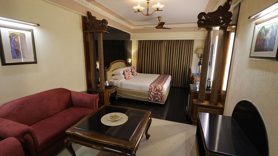 Overview image of Premium room at Hotel Amar with a bed, red sofa, table and long curtains.