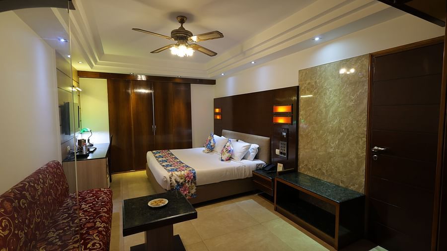 Side angle  image of Premium room at Hotel Amar with a bed, red sofa, table and long curtains.