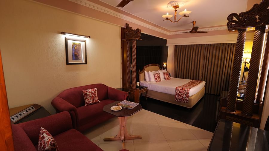 Overview image of Premium room at Hotel Amar with a bed, red sofa, table and long curtains.