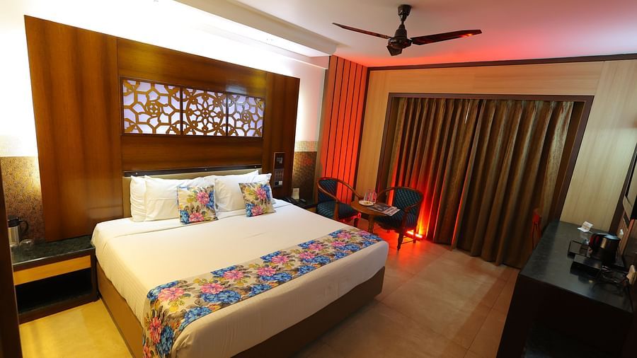  Overview image of a deluxe room at Hotel Amar with a bed, table, TV and huge window with curtains. 