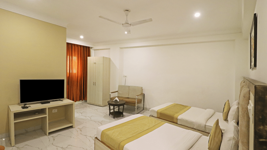 A twin bedroom at Hotel Apple Park Delhi featuring two single beds with lime green runners, a television on a stand, and a wardrobe in the corner.