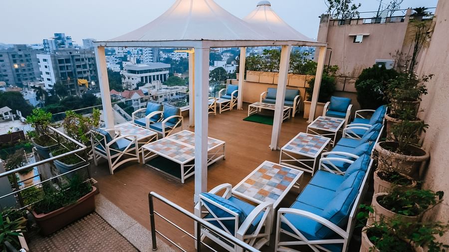 An outdoor dining setup at Hotel Ashok Nagpur featuring blue cushioned lounge chairs, potted plants, and a partially visible white canopy.