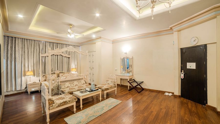 King Suite featuring a bed and a seating area with sofas and a coffee table, a wooden floor, and a door.- Hotel Ashok Nagpur