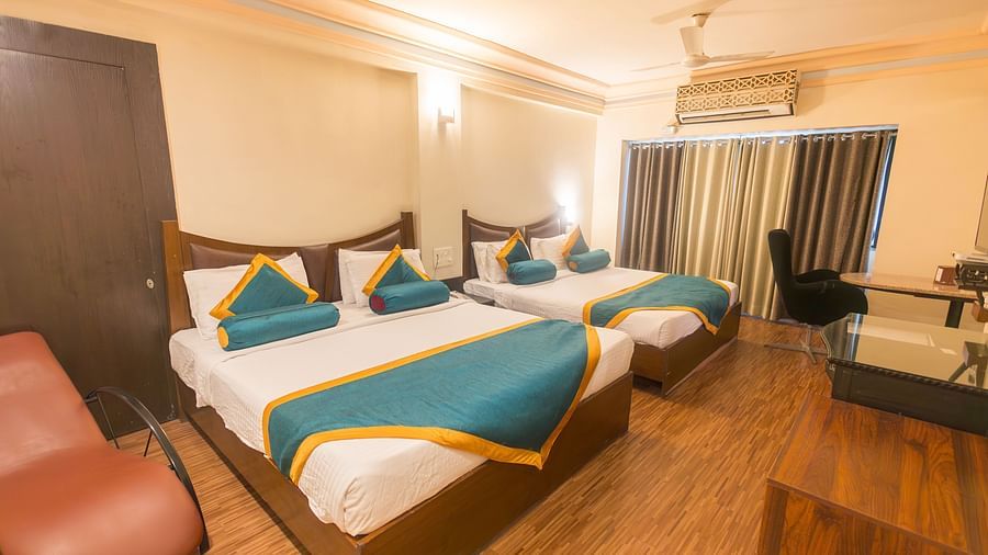 Family Room featuring two beds, a chair, and wooden flooring.- Hotel Ashok Nagpur