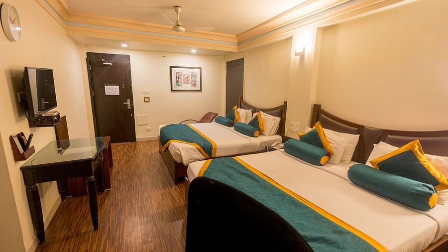 Family Room featuring two beds with white linens, teal and yellow accents, and dark wood headboards. - Hotel Ashok Nagpur