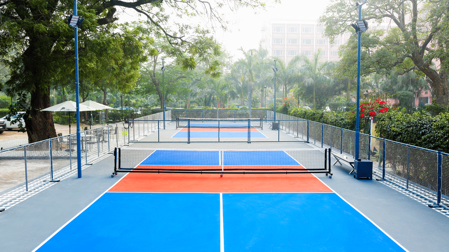 Symmetrical view of pickleball court with net and fencing in a green setting at Hotel Clarks Shiraz, Agra.
