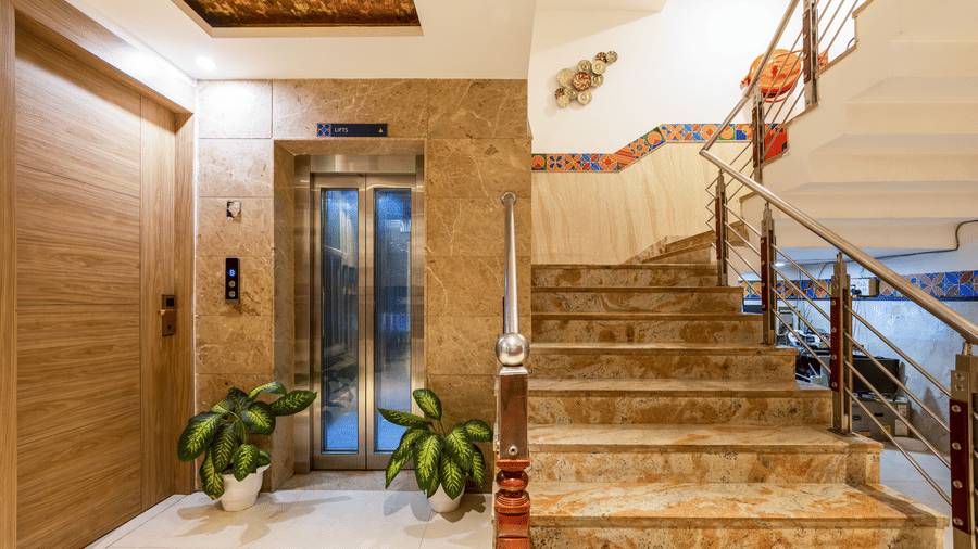 Lobby entrance of Hotel Corporate Suites featuring a lift, marble-effect wall panelling, and a wide staircase