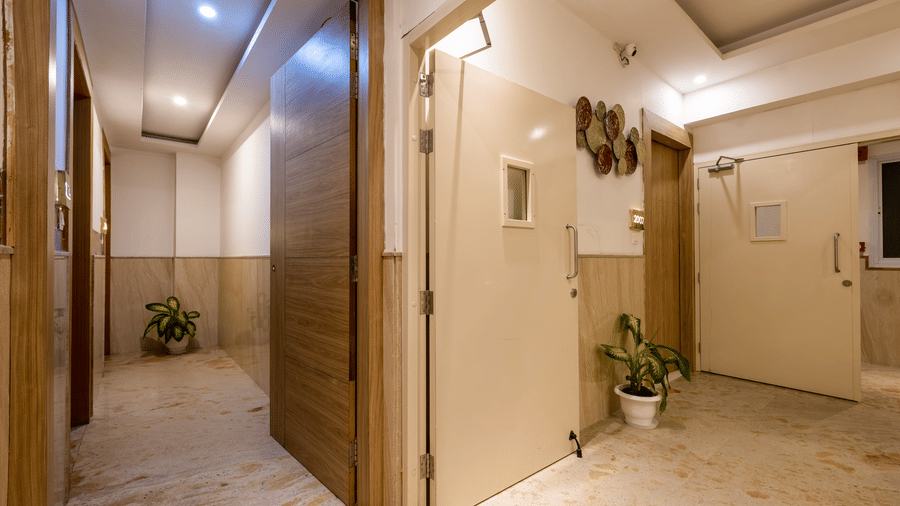 Corridor of Hotel Corporate Suites with polished marble floors, wooden panelling, and soft lighting leads towards an open door, revealing a glimpse of the building interior