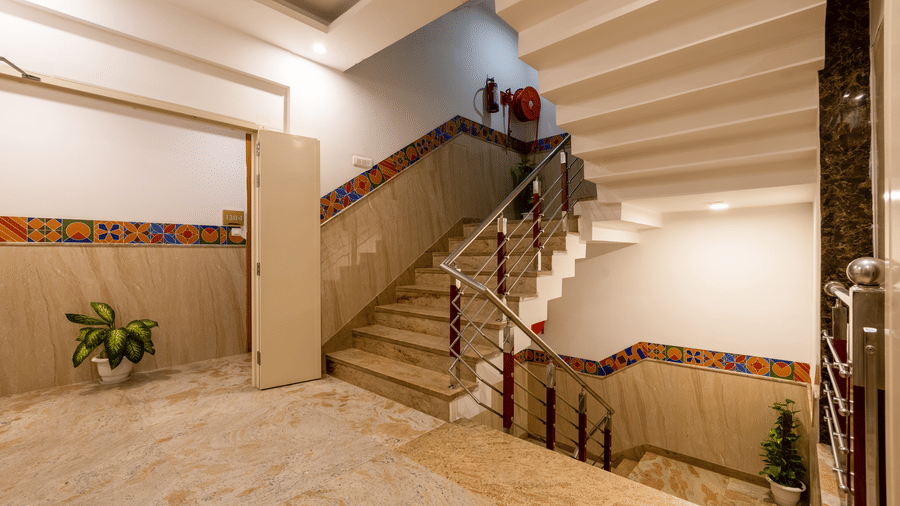 A staircase at Hotel Corporate Suites with a polished stone finish, complemented by a decorative wall pattern and bright ceiling lighting