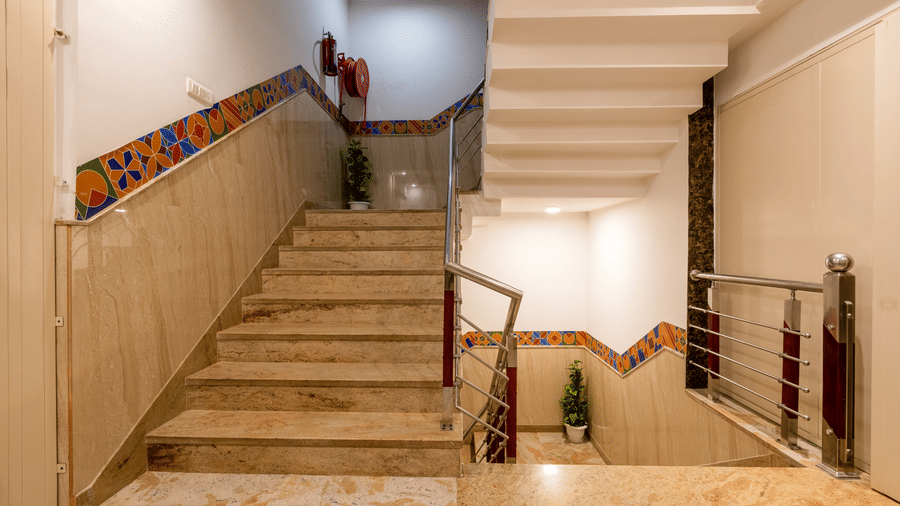 The staircase at Hotel Corporate Suites featuring marble steps with a steel balustrade, stylish wall trim with geometric colours, and a prominent red fire safety apparatus