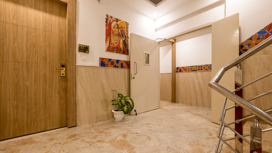 Corridor of Hotel Corporate Suites with a framed portrait, a house plant below, and a door leading to a room