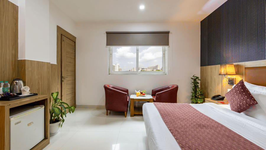 Deluxe Room at Hotel Corporate Suites featuring a plush bed with lamps over the nightstand and a seating space by the window