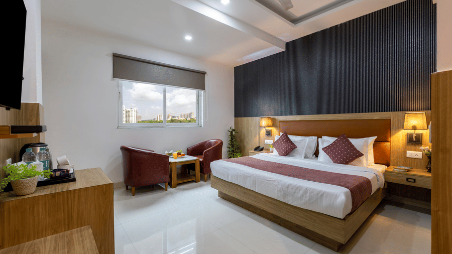 Deluxe Room at Hotel Corporate Suites featuring a plush bed with lamps lit on both sides above the nightstands and a seating space next to the window