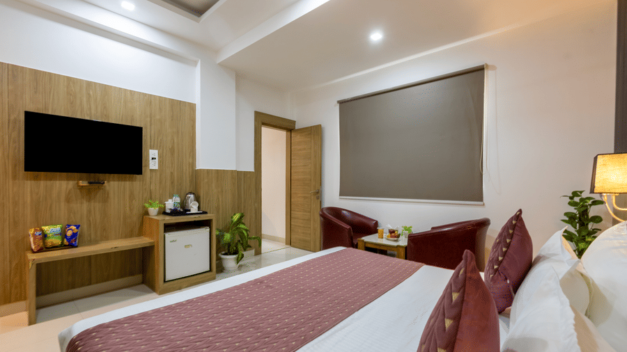 Deluxe Room showcasing a double bed facing a TV on the wall with snacks, tea and coffee maker, and a minibar below on the counter