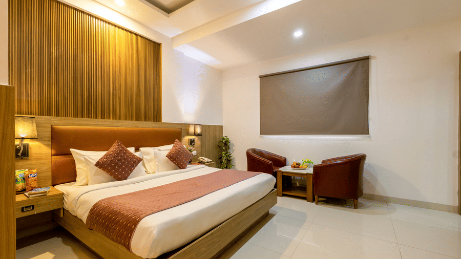 Deluxe Room featuring a double bed against a patterned wall and a seating space next to a closed window at Hotel Corporate Suites