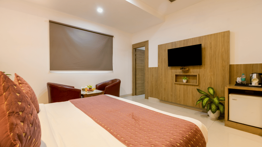 Deluxe Room featuring a double bed with cushions and bed runner facing the wall-mounted TV with a seating space by the window at Hotel Corporate Suites
