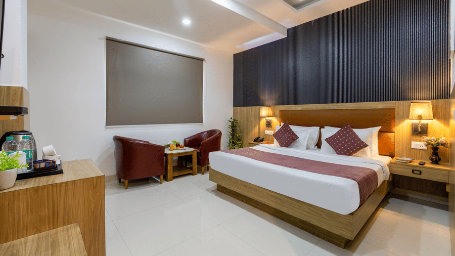 Deluxe Room featuring a double bed with lamps lit on both sides and a seating space by the bed next to a closed window at Hotel Corporate Suites