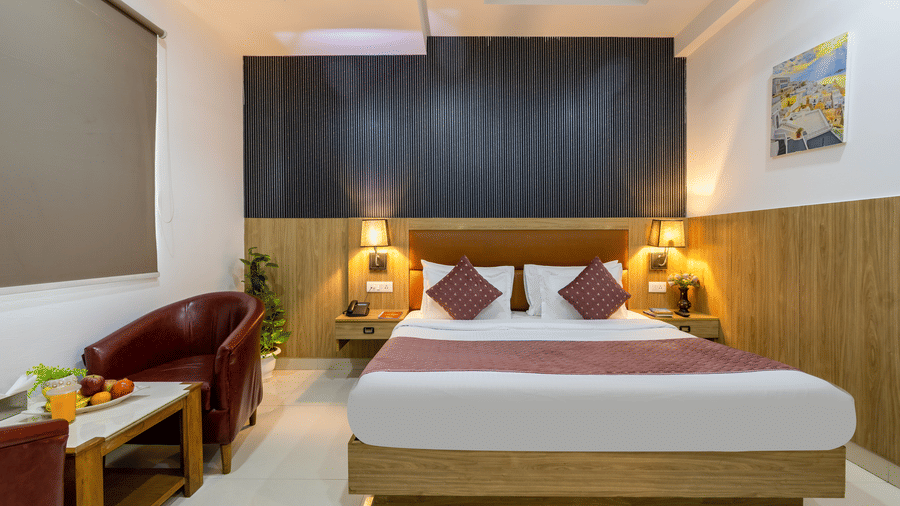 Deluxe room highlighting a bed with maroon cushions, modern black slat wall detailing, and a sitting area with leather armchairs and refreshments at Hotel Corporate Suites
