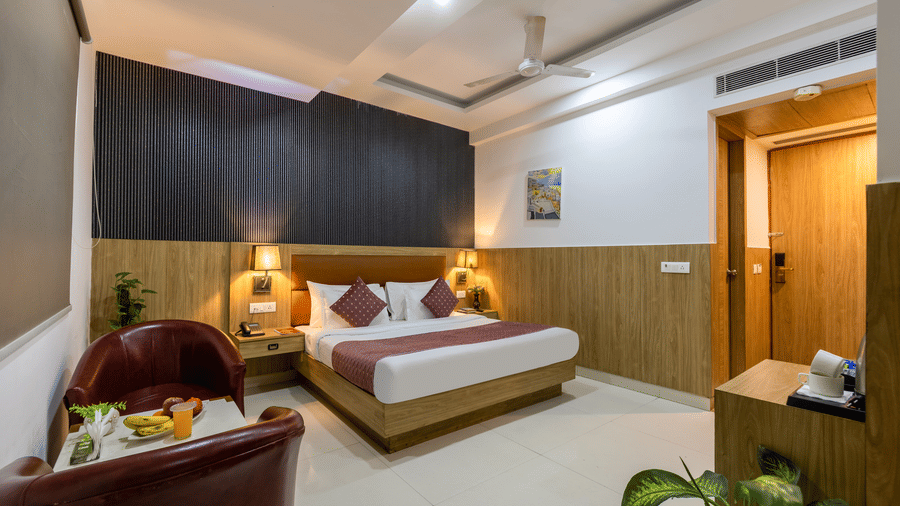 Deluxe Room featuring a double bed, warm ambient lighting, and a cosy seating area with fruits at Hotel Corporate Suites